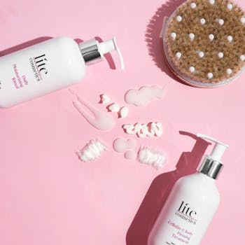 Inicio Flatlay of skincare products on pink background featuring lotion bottles and a body brush.